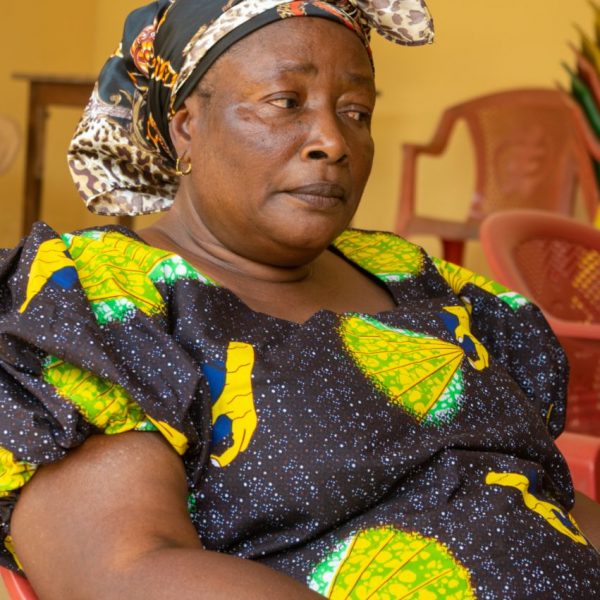 A widow in patterned kente-print cloth waits at the community centre