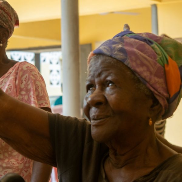 An elderly widow raises her hand in response during the community meeting