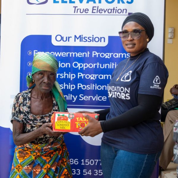 A Foundation Elevators volunteer presenting tinned goods to a beneficiary