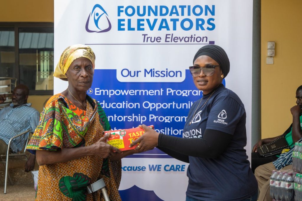 A Foundation Elevators volunteer handing supplies to a widow in front of the mission banner